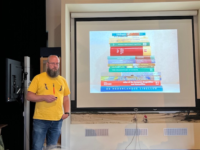 Een man geeft een presentatie met een projectie van een stapel boeken op het scherm.