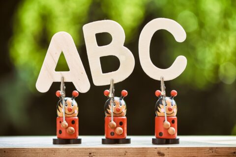Drie houten figuren houden de letters "ABC" vast op een tafel met groene achtergrond.