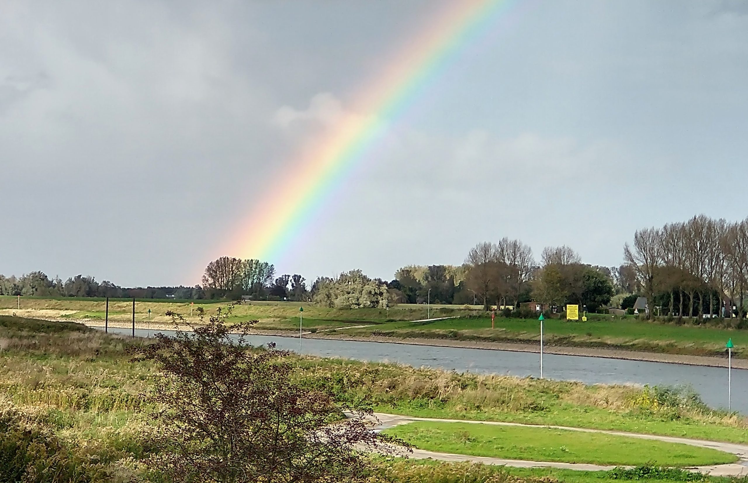 Een regenboog boven een rivierlandschap met bomen op de achtergrond.