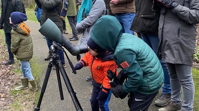 Kinderen en volwassenen kijken door een telescoop in een park.