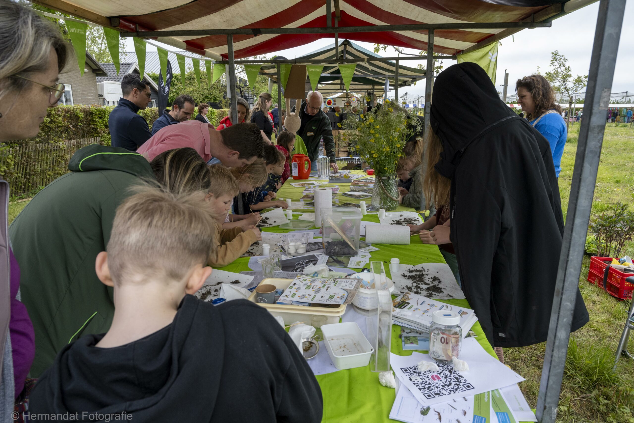 Mensen doen mee aan een natuurworkshop onder een tent, met folders en materialen op tafels.