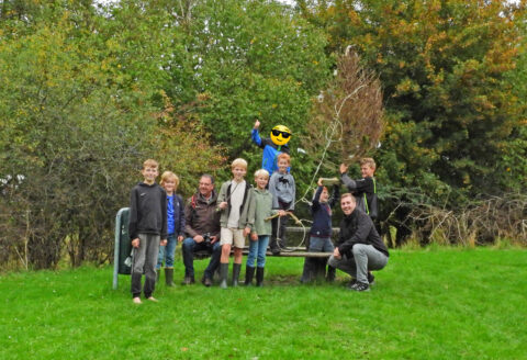 Groep mensen en kinderen buiten, met een versierde boom en groene achtergrond.