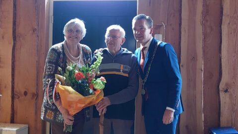 Drie mensen poseren samen, een vrouw met bloemen, een man met een medaille en een man in pak.