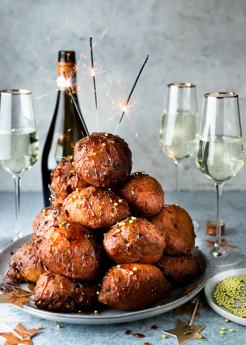 Een stapel oliebollen met sterretjes, omringd door champagneglazen en een fles wijn.
