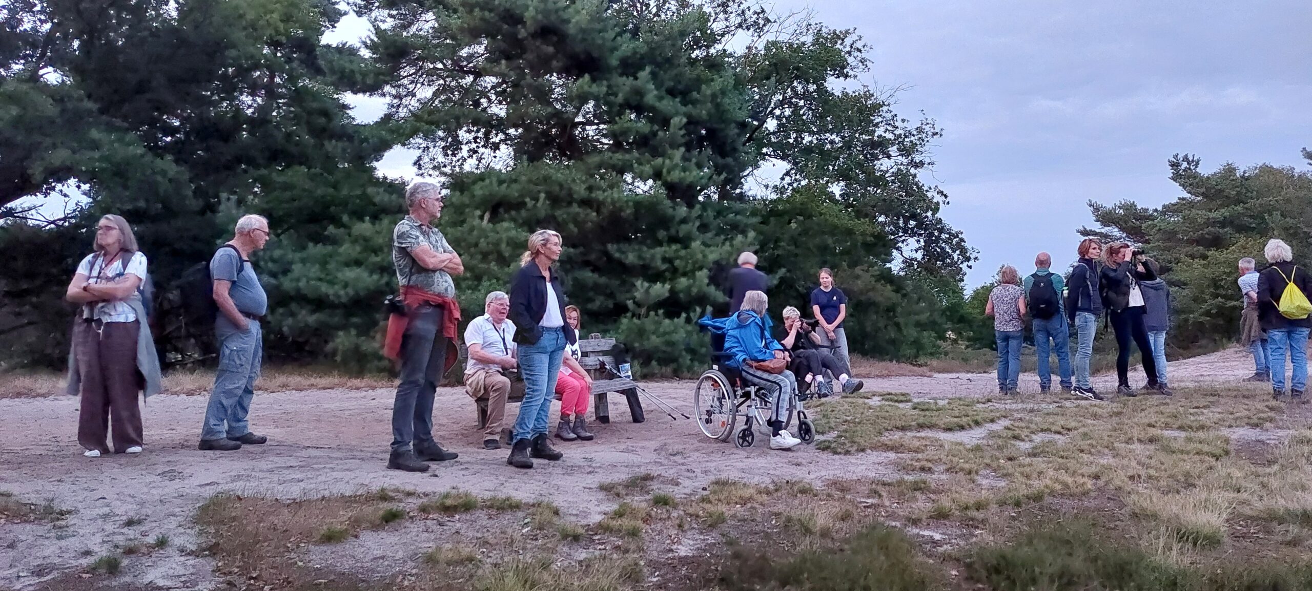 Een groep mensen staat en zit in een natuurgebied, omringd door bomen.