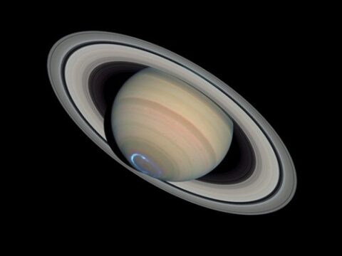 Saturnus met zijn ringen en een blauw aurora boven de zuidpool op een zwarte achtergrond.