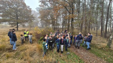 Groep scouts en begeleiders verzamelen zich in een bosrijke omgeving in de herfst.