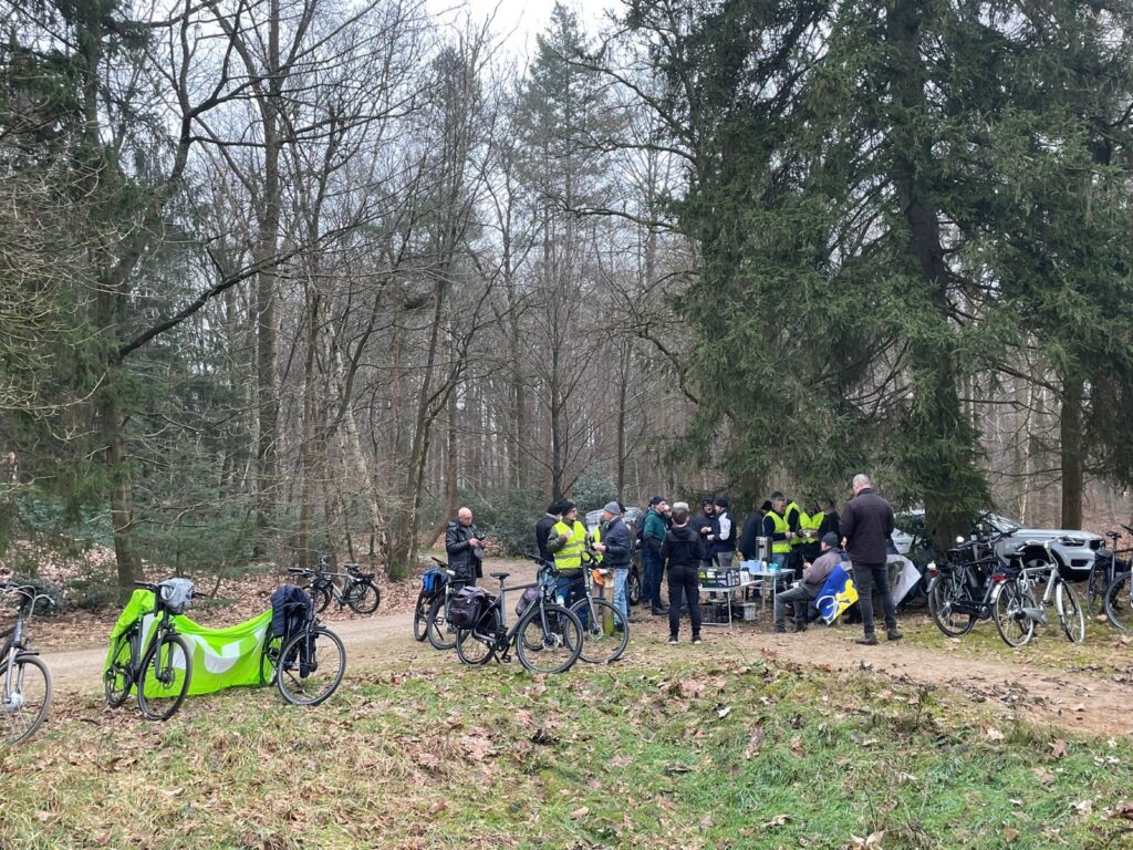 Mensen verzamelen zich met fietsen en tafels in een bosrijke omgeving.