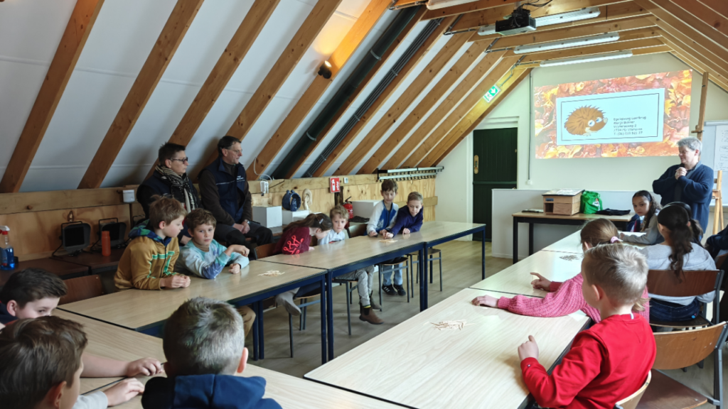 Kinderen zitten in een klaslokaal met een projectie van een egel op het scherm.