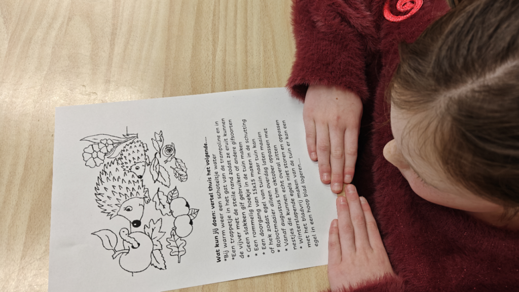 Een kind leest een vel papier met een tekening van een egel en begeleidende tekst.
