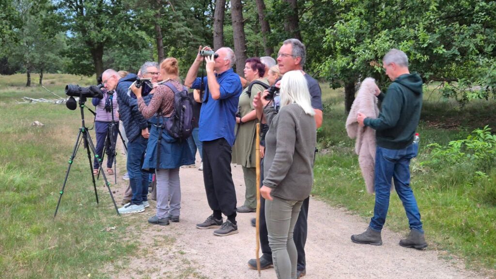 Een groep mensen op een pad in een bos observeert met verrekijkers en telescopen.
