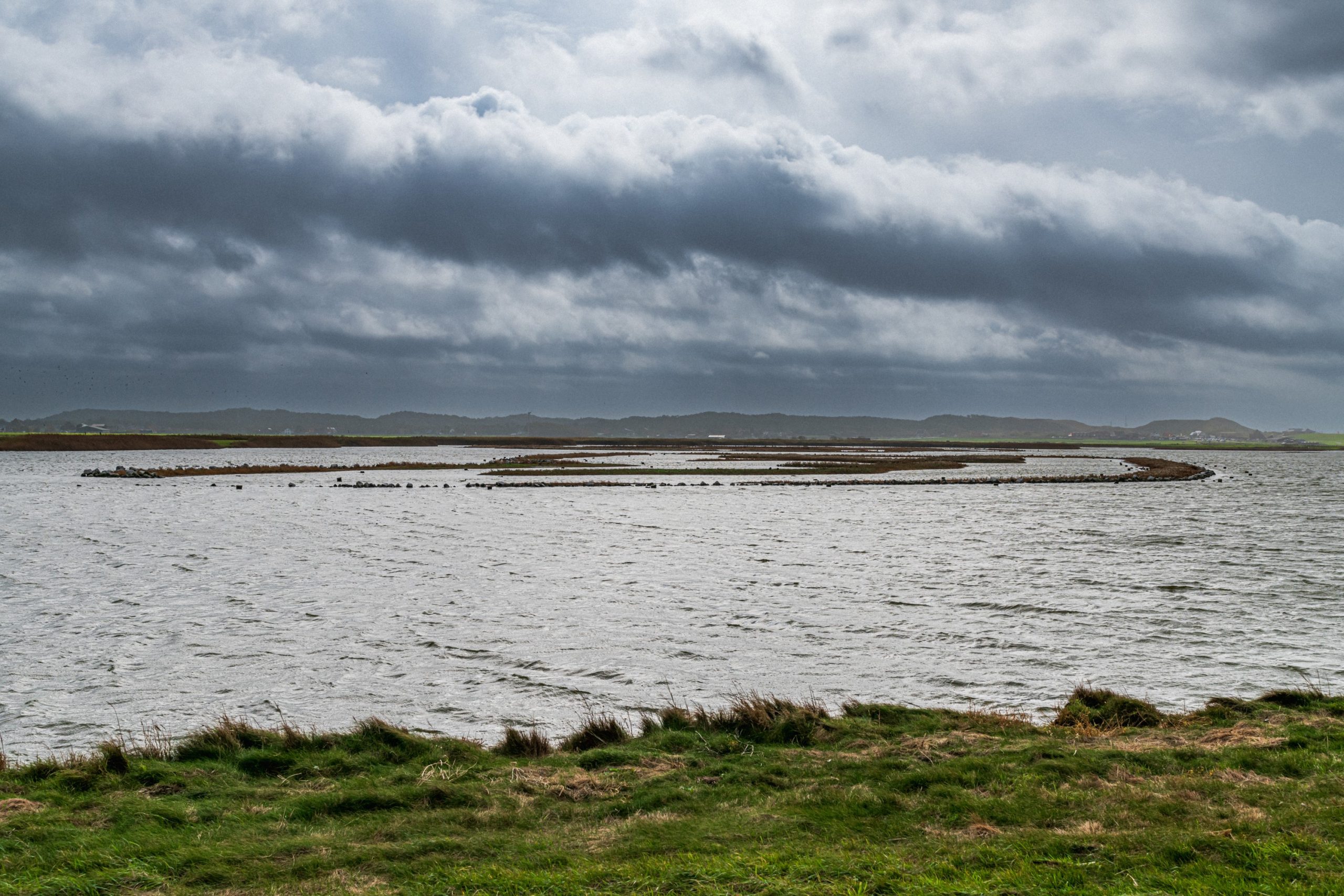 Winderig landschap met water, bochtige kustlijn en donkere wolken.