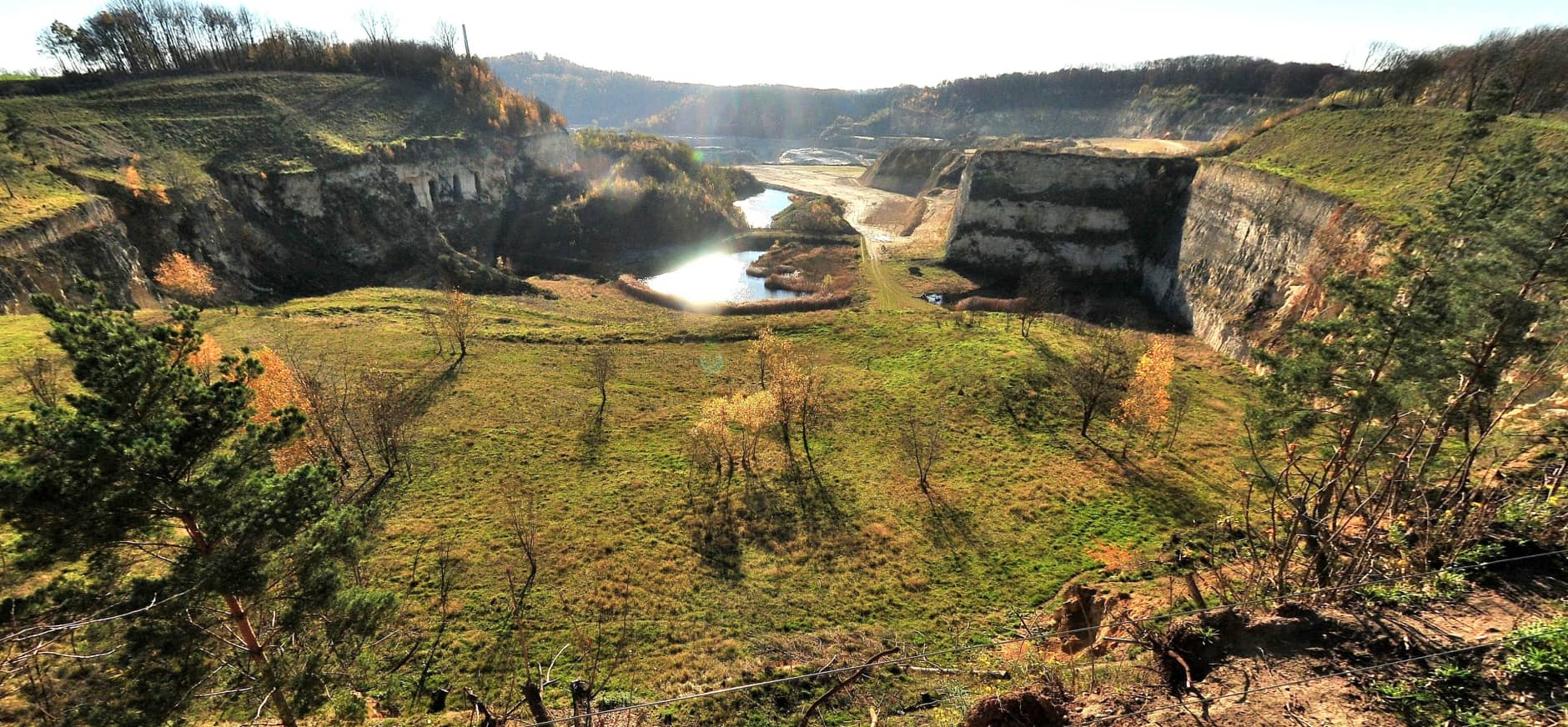 Groen dal met verspreide bomen en plassen, omgeven door steile rotswanden en bossen.