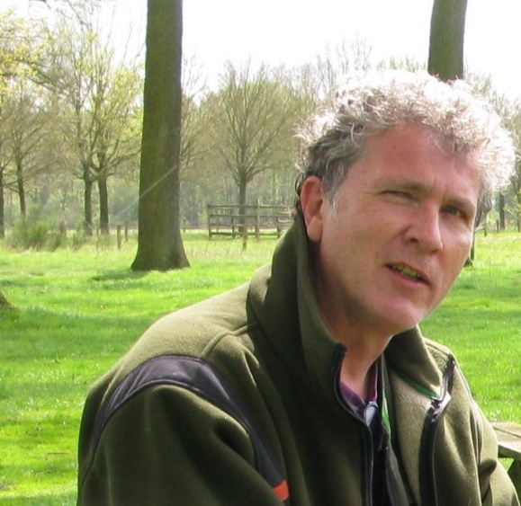 Sorry, ik weet niet wie de persoon is in de afbeelding. Een man zit buiten in een groene omgeving met bomen.