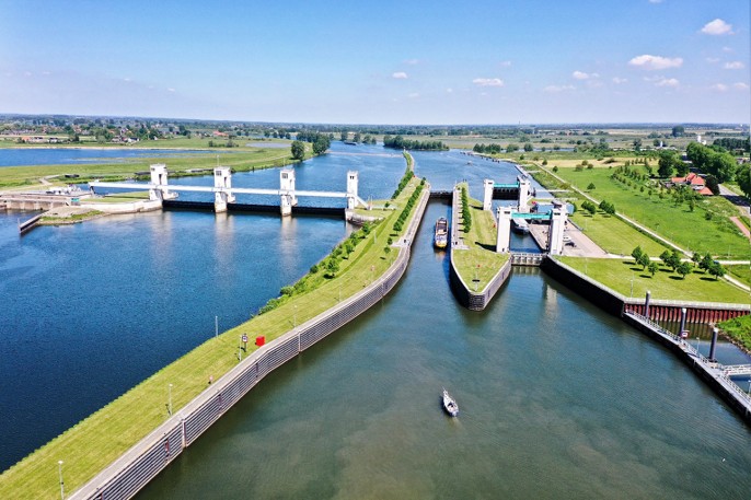 Luchtfoto van een sluiscomplex en rivier, met groene oevers en een blauwe lucht.