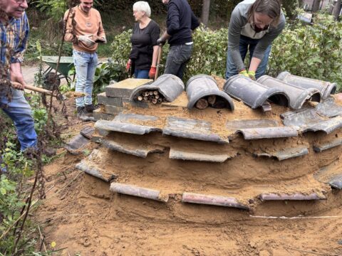 Mensen bouwen een insectenhotel met dakpannen en bakstenen in een tuin.