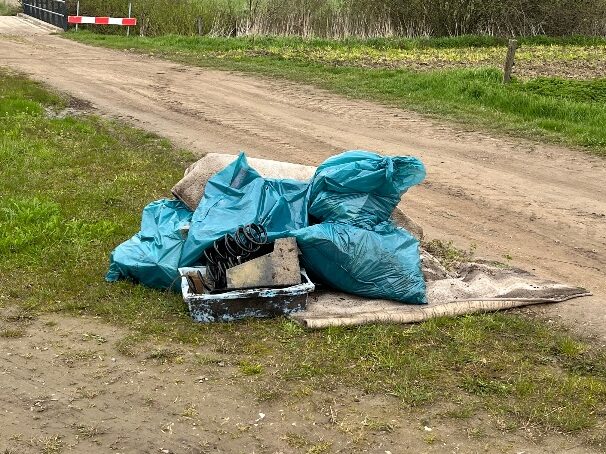 Afval met blauwe zakken en autoveer langs een onverharde weg bij groen landschap.