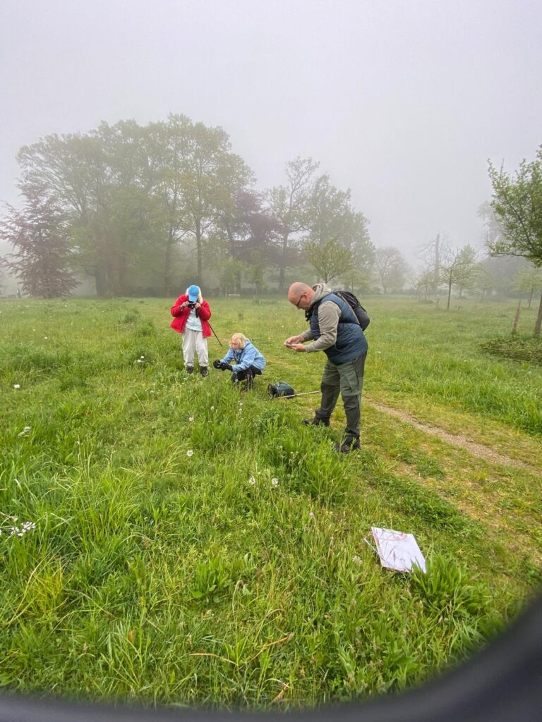 Mensen onderzoeken gras in een mistig veld met bomen op de achtergrond.