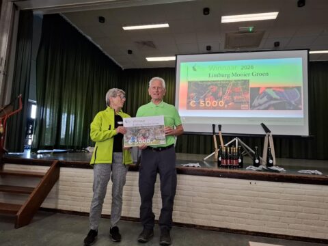 Twee mensen presenteren een cheque van €5000 op een podium tijdens een prijsuitreiking.