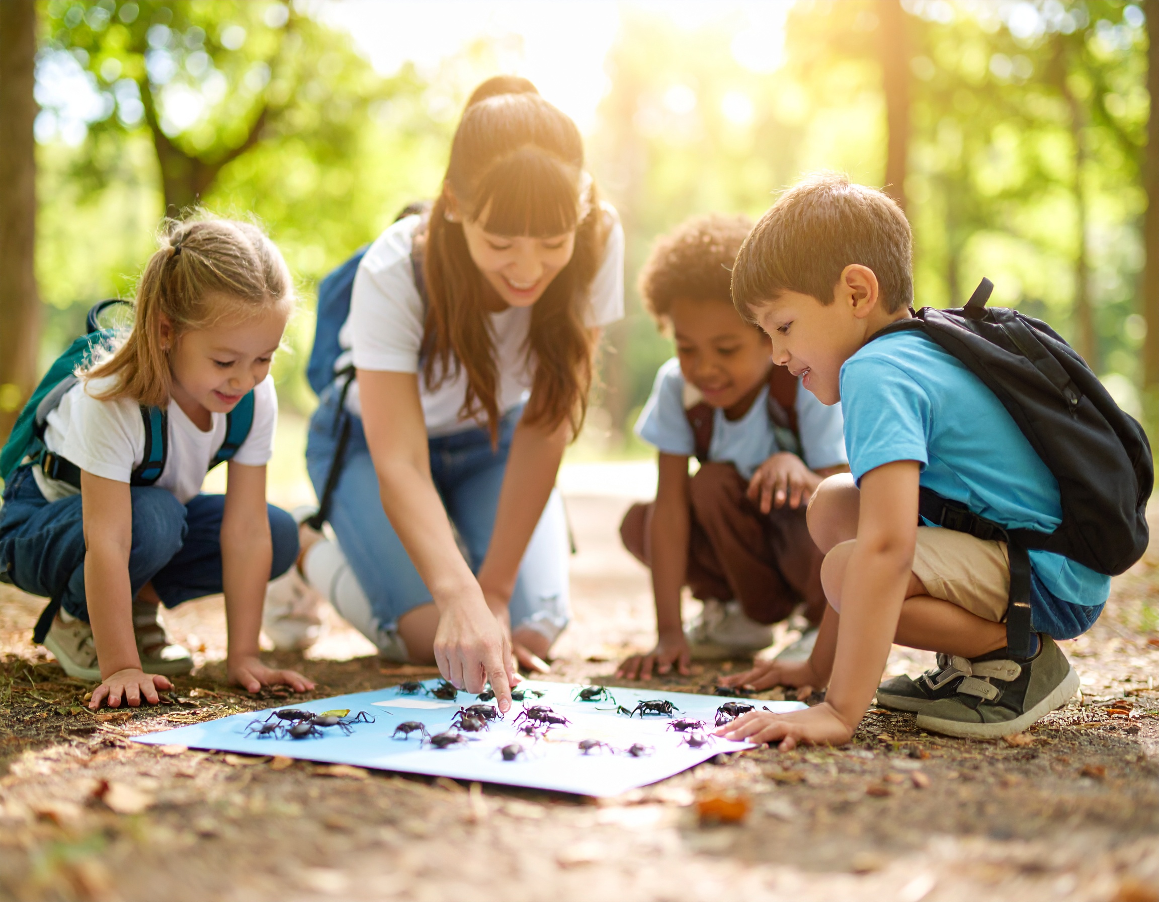 Kinderen en een volwassene bestuderen insecten op een blauw bord in een bosrijke omgeving.