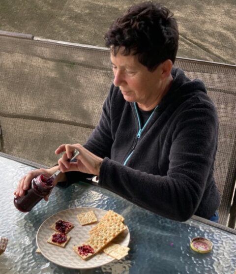 Persoon smeert jam op crackers aan een glazen tafel buiten.