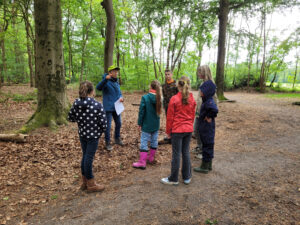 Groep kinderen luistert naar gids in het bos tijdens een educatieve excursie.