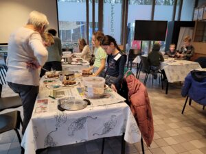 Groep kinderen en een volwassene bezig met knutselactiviteiten aan tafels in een klaslokaal.