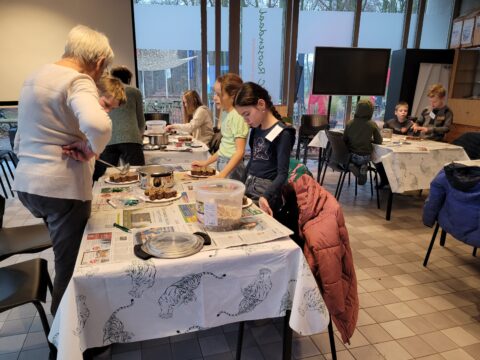 Groep kinderen en een volwassene bezig met knutselactiviteiten aan tafels in een klaslokaal.