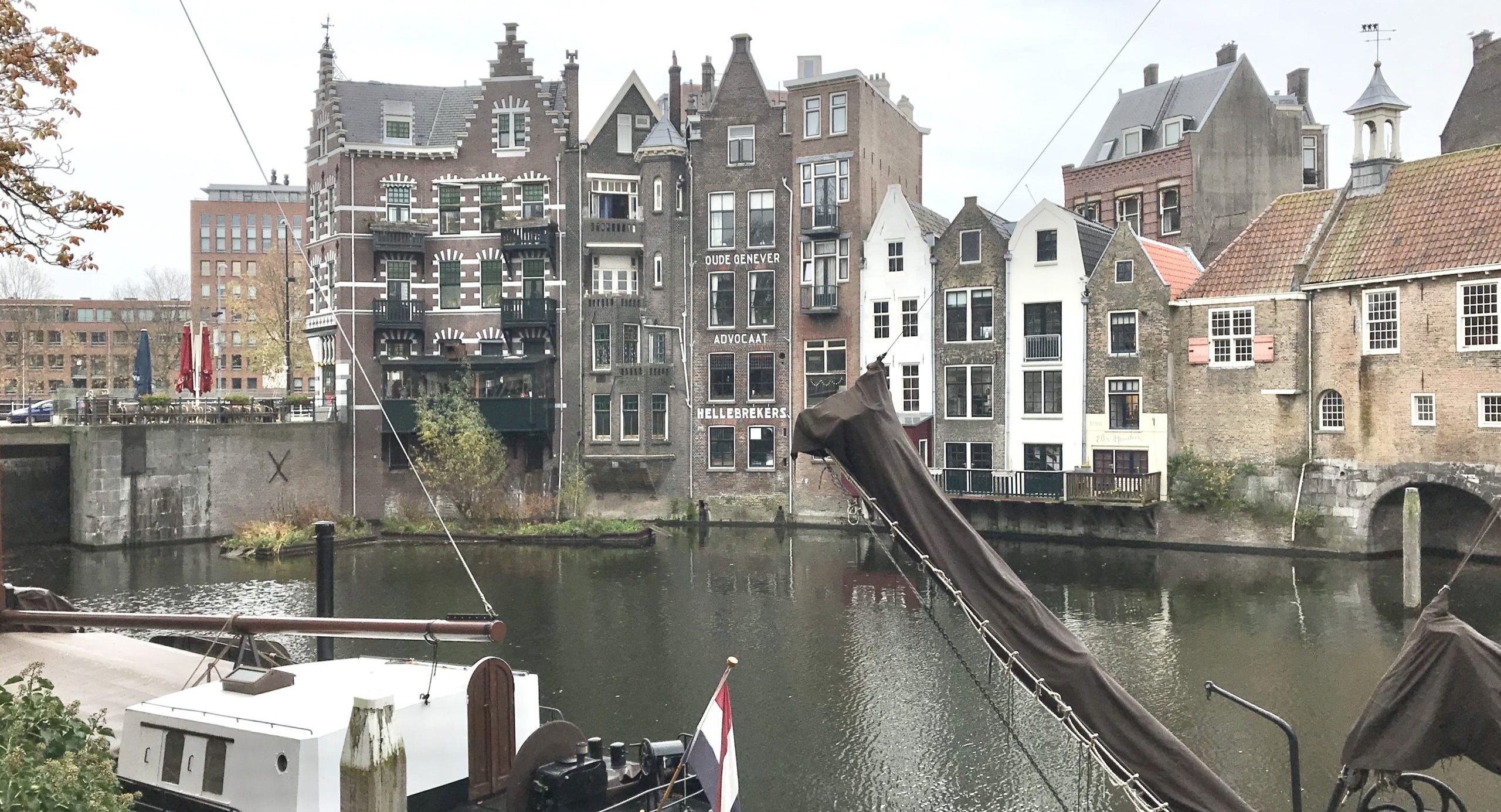 Historische gebouwen aan een rustige gracht met een aangemeerde boot en Nederlandse vlag.