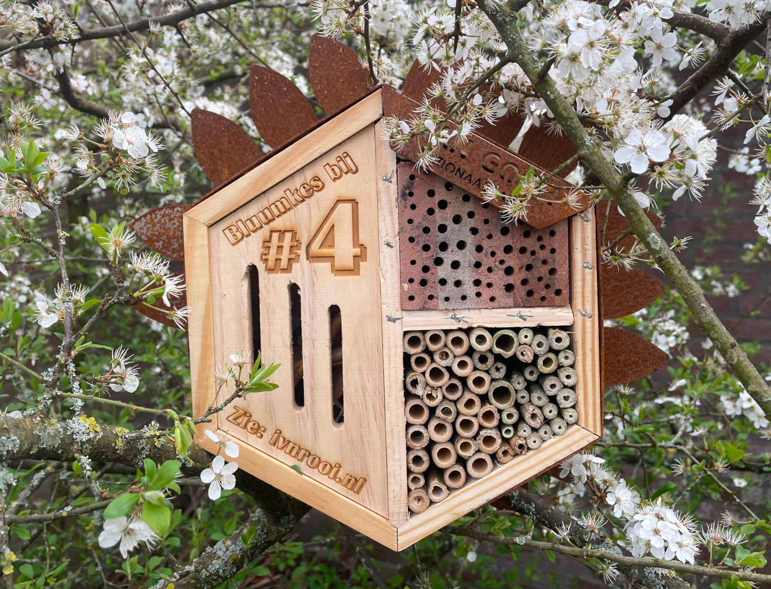 Bijenhotel met tekst "Bluumkes bij #4" in een bloesemtak.