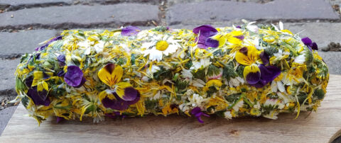 Rol met eetbare bloemen en kruiden op houten plank.