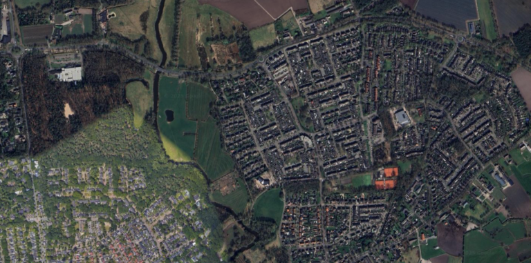 Luchtfoto van een uitgestrekte woonwijk met groen, wegen en nabijgelegen velden.