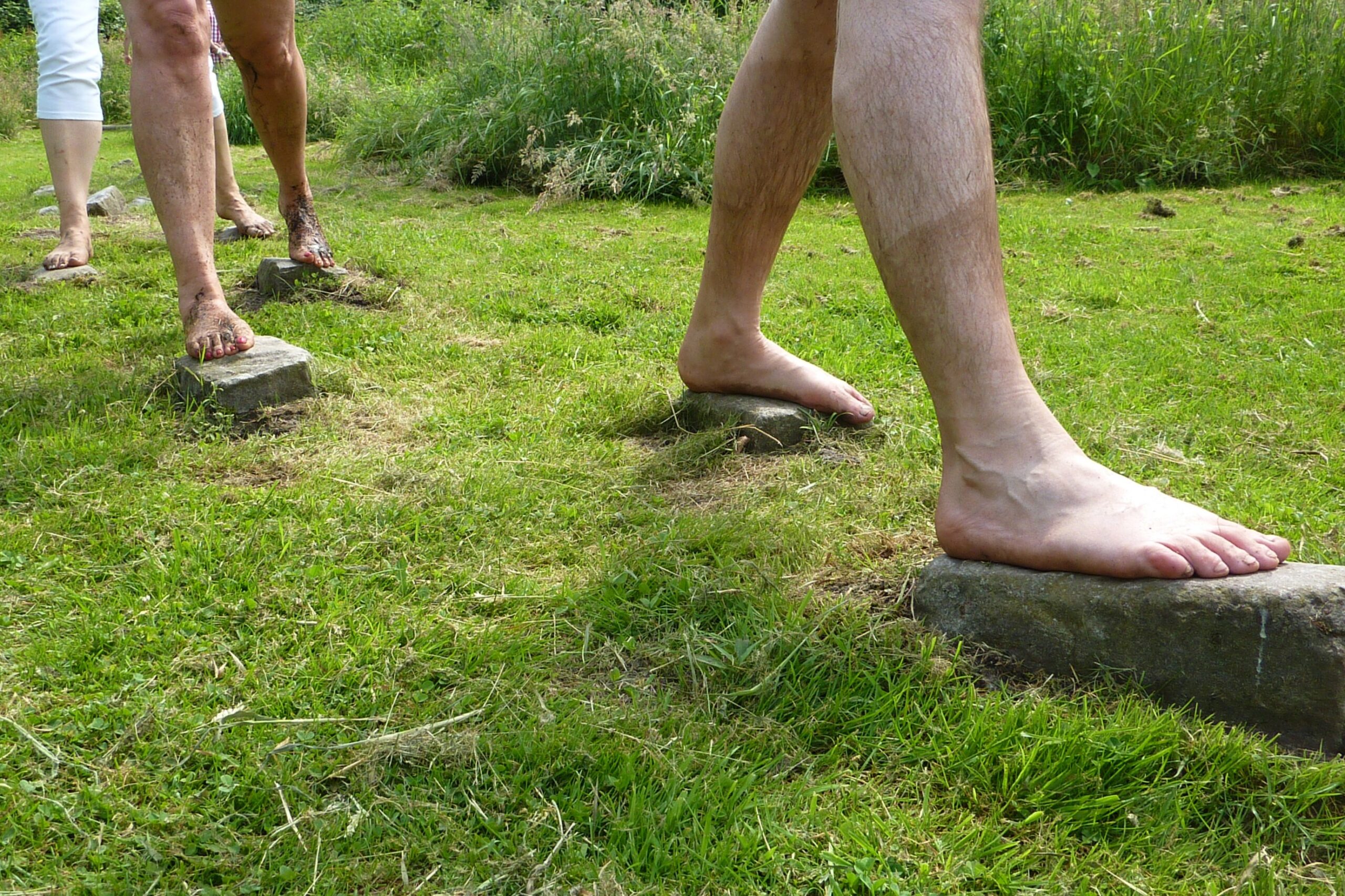 Blote voeten lopen over stenen in gras, met modderige en schone voeten zichtbaar.