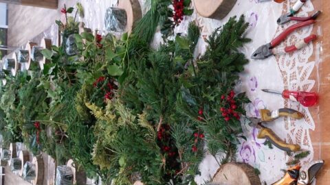 Takjes groen en rode bessen op een tafel met gereedschap en boomschijven voor kerstdecoratie.