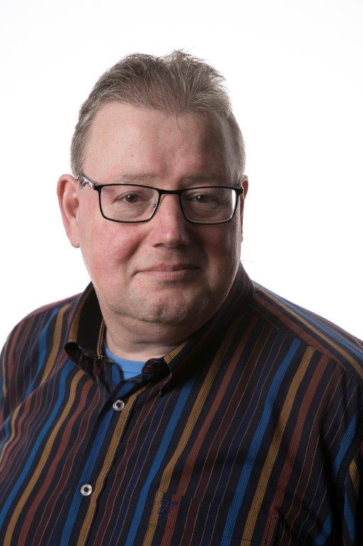 Man met bril en gestreepte blouse kijkt naar de camera tegen een neutrale, witte achtergrond.