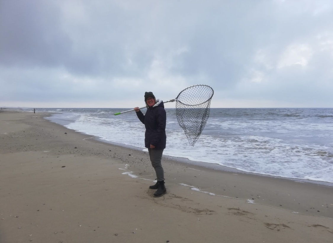 Persoon met visnet op een lege, bewolkte strandlijn naast de zee.