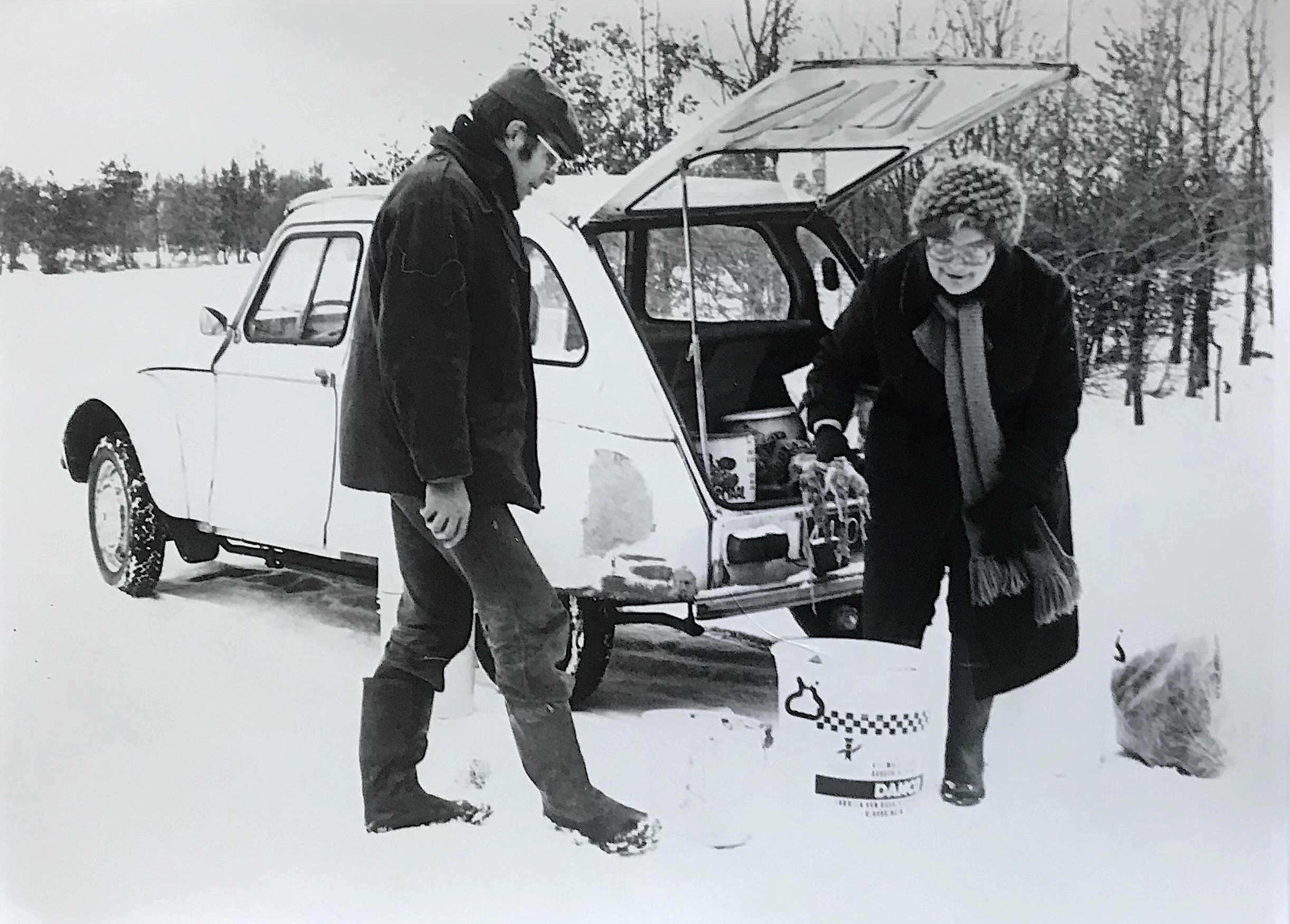 Twee mensen bij een auto in een besneeuwd landschap, bezig met spullen uitladen.