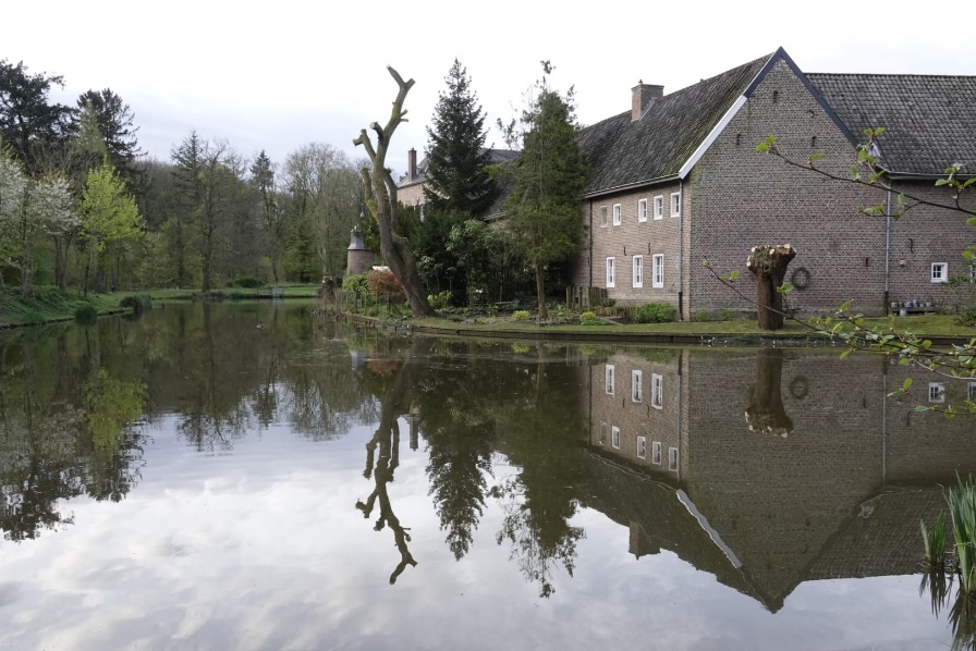 Bakstenen huis weerspiegeld in een rustige vijver, omgeven door bomen.