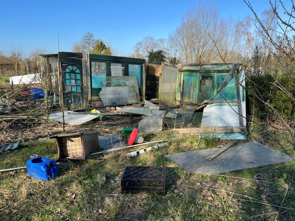 Vervallen tuinhuisje met verspreid afval op overwoekerd grasveld.