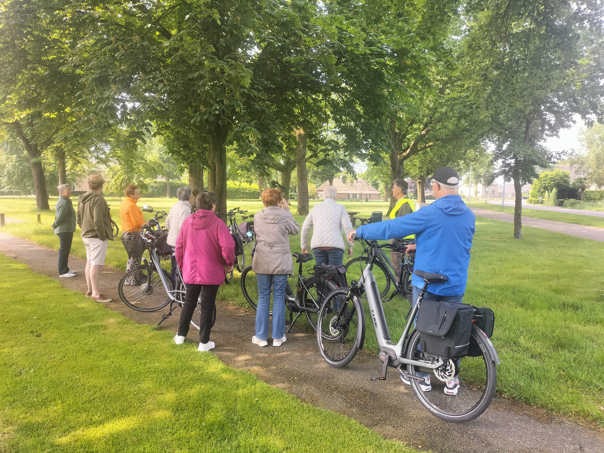 Groep mensen met fietsen stopt onder bomen in een parkachtige omgeving.