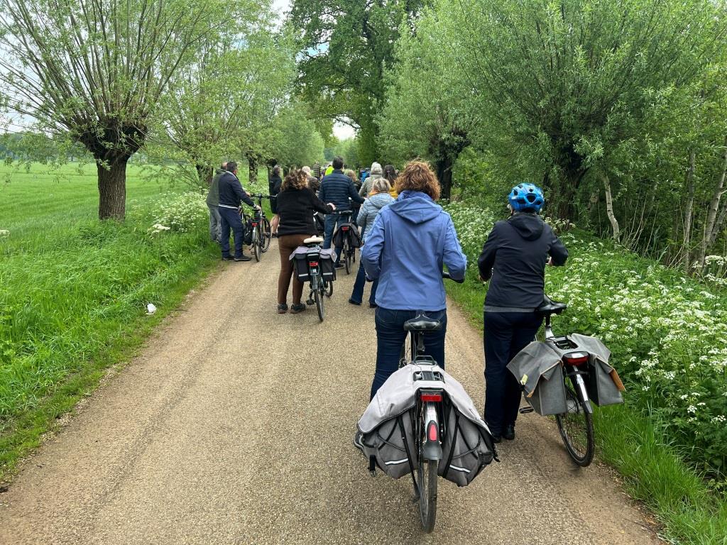 Groep fietsers rijdt over een landelijk paadje omringd door bomen en groen.