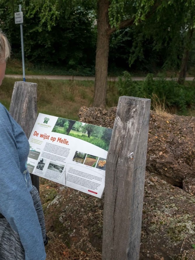 Een persoon leest een informatief bord over "De wijst op Melle" in een bosrijke omgeving.