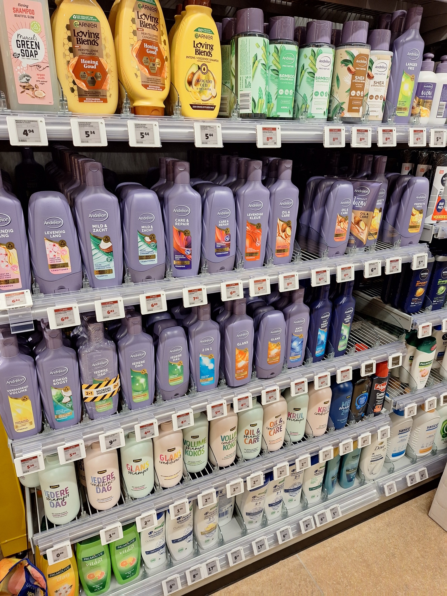 Shampoo- en conditionerflessen staan uitgestald in supermarkt, met diverse merken en prijsetiketten.