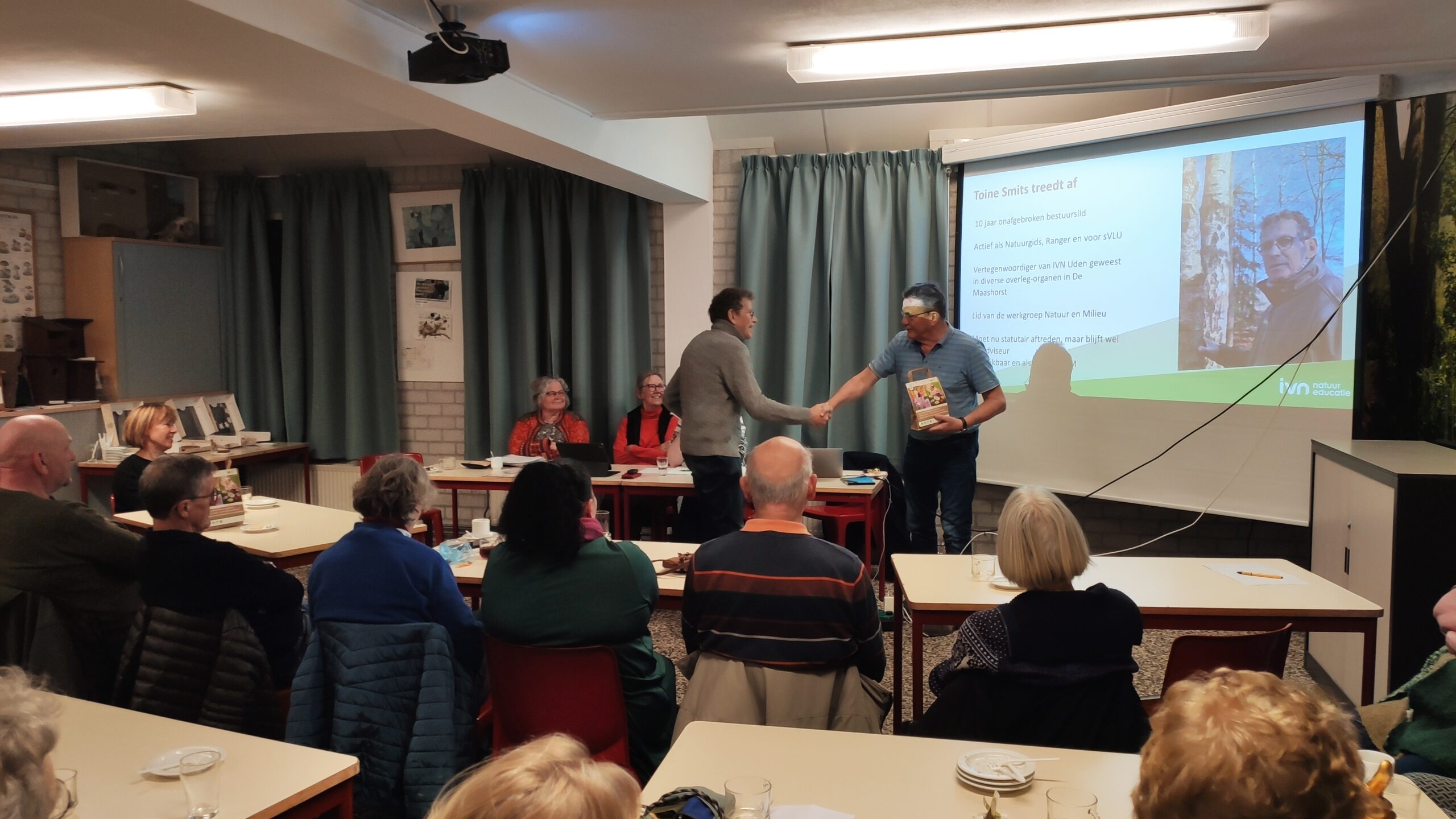 Een man krijgt een boek bij een afscheidspresentatie voor een groep in een vergaderruimte.