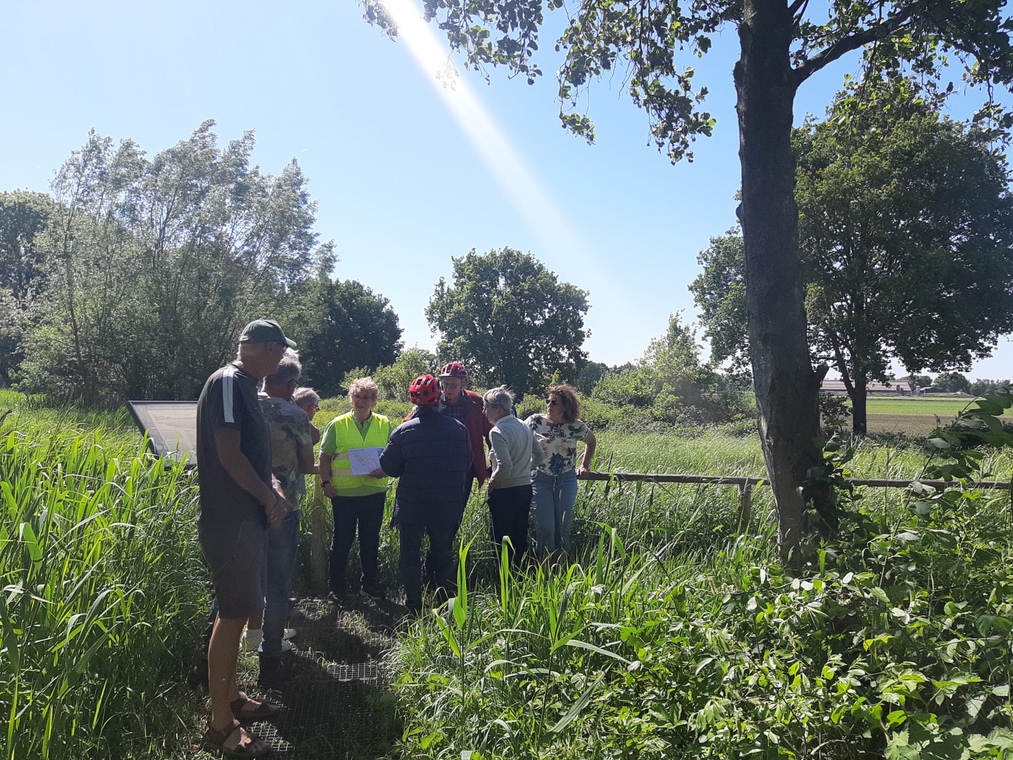 Groep mensen verzameld in een groen natuurgebied onder een blauwe hemel.