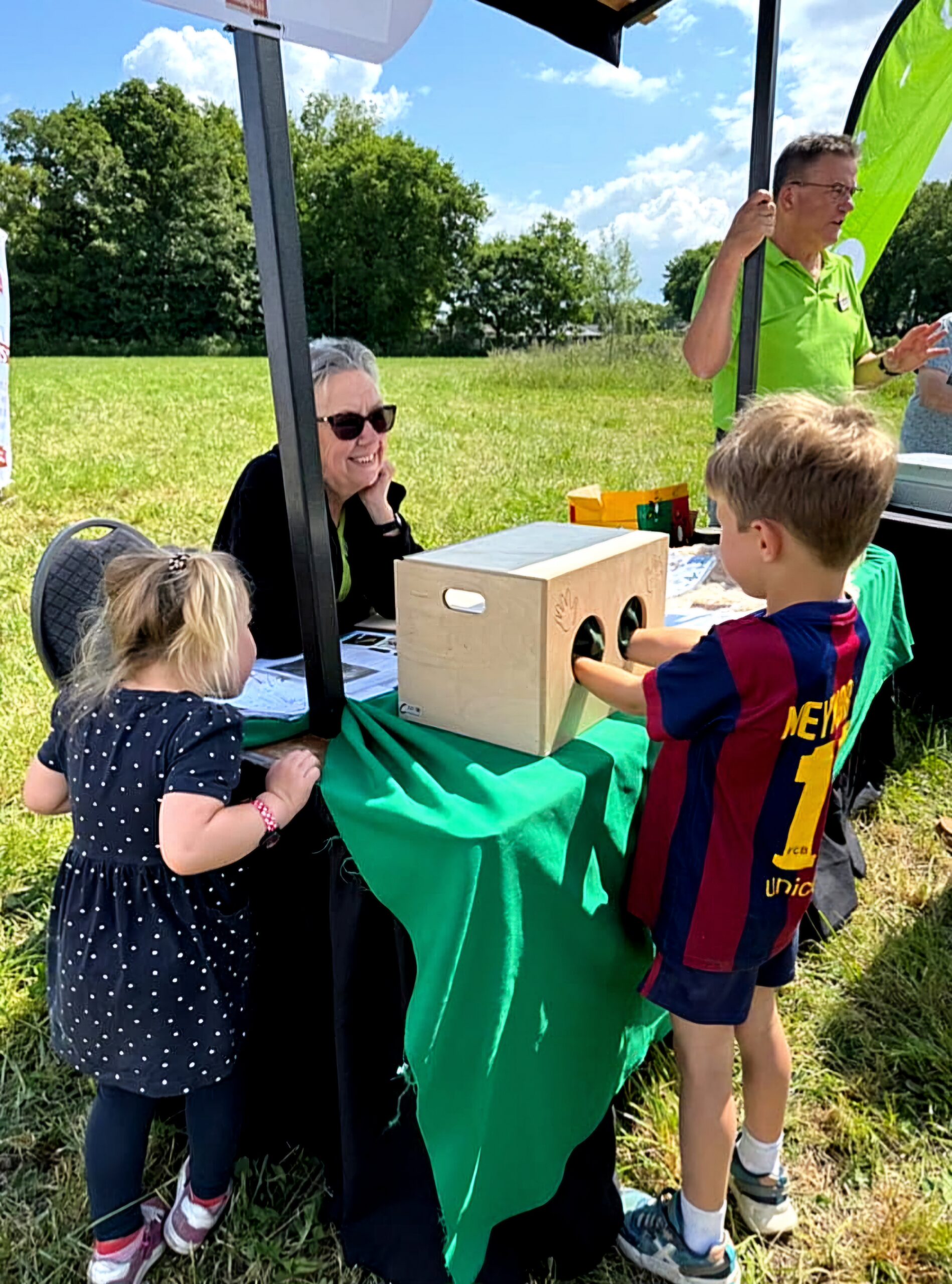 Kinderen experimenteren bij een informatietafel buiten, met een houten voeldoos.