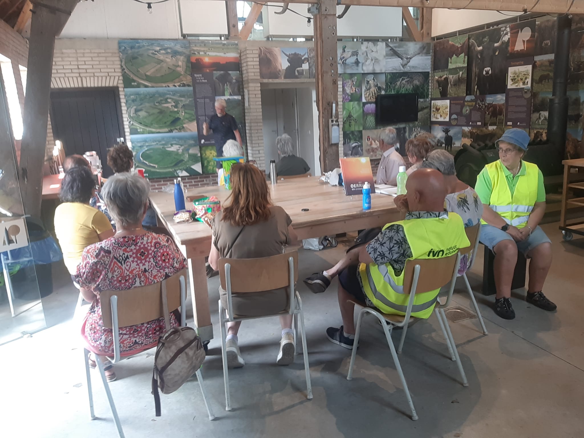 Een groep mensen luistert naar een spreker in een zaal met natuurposters.