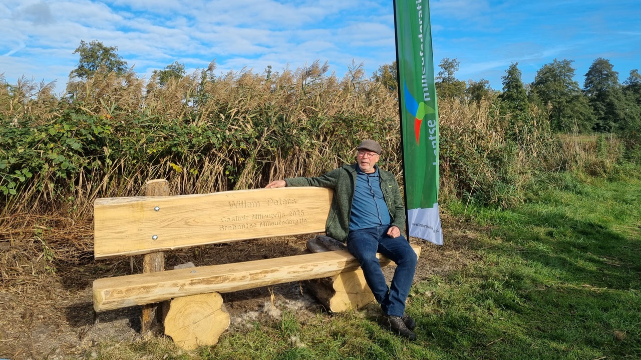 Man zit op een houten bank met inscriptie naast een groene vlag in een natuurlijke omgeving.
