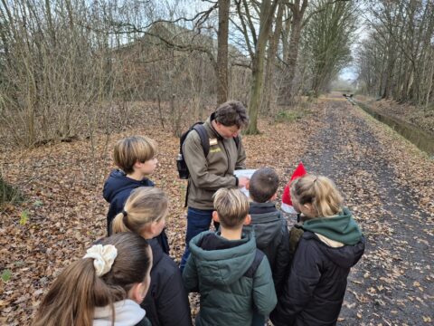 Groep kinderen en volwassene bekijken een kaart of document op een bosachtig pad in de herfst.