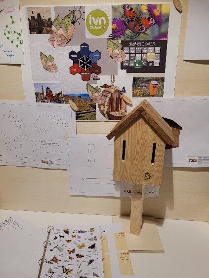 Knutselwerkplek met vogelhuisje, posters over natuurthema’s en tekeningen van vlinders op de achtergrond.